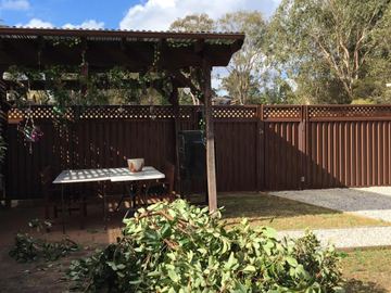 The scene shows a charcoal corrugated steel fence where lattice tops the panels, sleepers form the base.