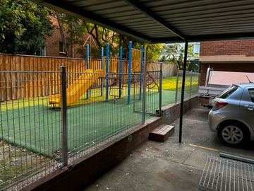 Matte black posts and rails frame a tight weldmesh centre section along a garden boundary under trees.