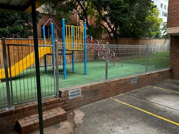 Silver mesh infill sits between black posts above a timber sleeper plinth beside paving and planting.