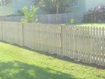 The scene shows a light grey corrugated steel fence where garden beds sit at the base.