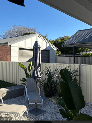 Cream Colorbond privacy fence enclosing a paved courtyard with lounge chairs