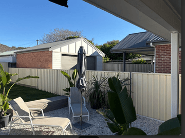 Cream Colorbond privacy fence enclosing a paved courtyard with lounge chairs