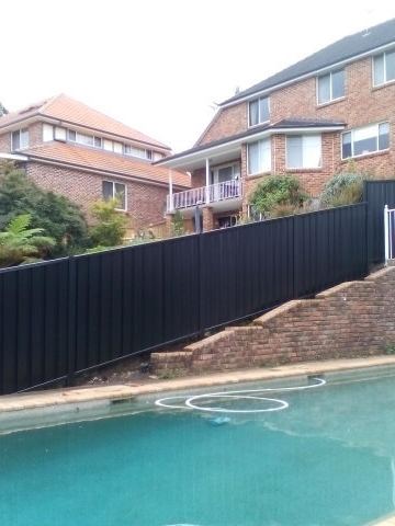 Black Colorbond privacy fence above a swimming pool on a stone retaining wall