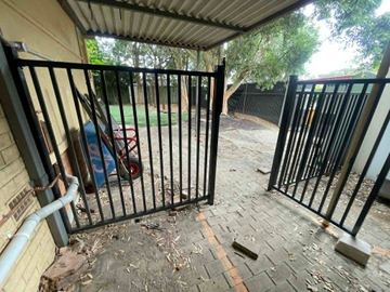 Black tubular double gate under a patio opening onto a paved courtyard