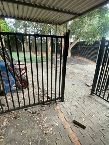 Black tubular double gate under a patio opening onto a paved courtyard