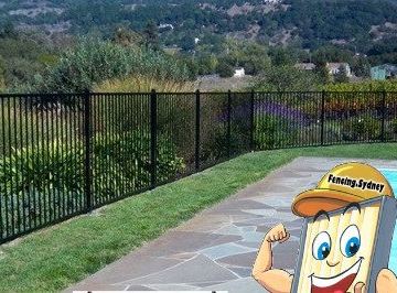 Black tubular fence running beside a swimming pool and a stone path