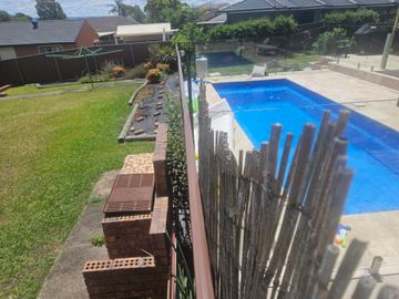 Backyard swimming pool photographed from above with a dark boundary fence beyond