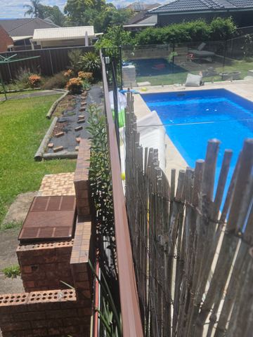 Backyard swimming pool photographed from above with a dark boundary fence beyond