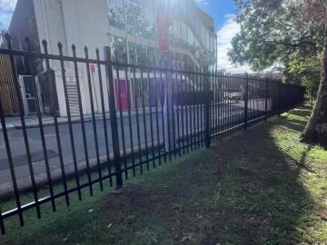 Black spear-top panels stepping along sloping grass beside a commercial driveway.