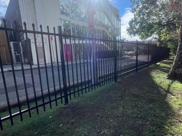 Spear-top steel fencing separating lawn from an apartment block car park.
