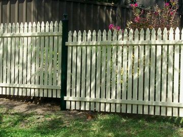 Cream pointed pickets on heritage-green posts step beside lawn with charcoal corrugated fencing and shrubs behind.