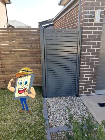 Charcoal horizontal slat gate sits on white pebbles between brown brick and timber slat fencing near outdoor lighting.