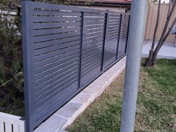 Horizontal aluminium slats mounted on a concrete block wall above a paved patio.