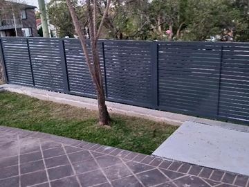 Dark horizontal slats running along a timber deck with garden planting behind.