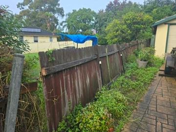 Weathered timber paling fence leaning along a garden boundary beside a paved path