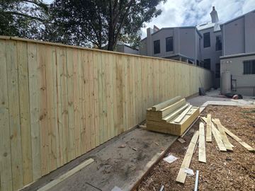 New treated pine paling fence running beside a townhouse with leftover palings stacked on the ground
