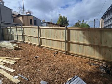 New treated pine paling fence with steel posts standing on a mulched yard with leftover palings on the ground
