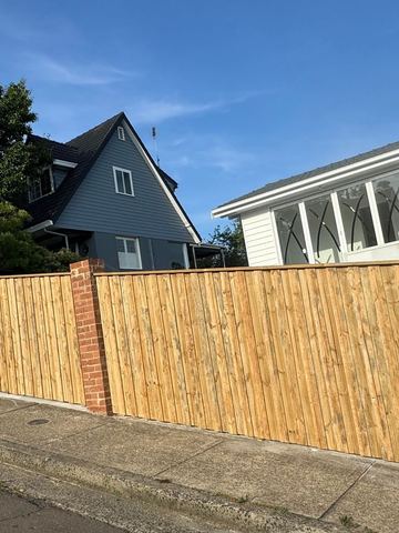 Treated pine paling fence set between brick piers along a street footpath