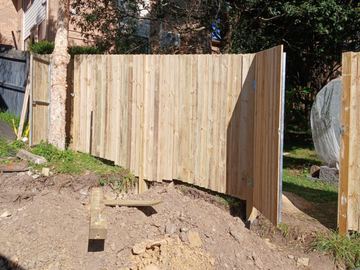 A treated pine paling fence standing on a timber sleeper retaining wall