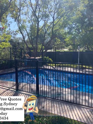 Black picket pool panels and a latched gate surround blue pool water on stone coping with blossom petals nearby.